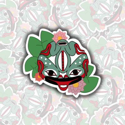 This sticker is of a green frog with red accents. It has a red tongue sticking out. around the frog are green leaves and pink flowers with yellow centers.