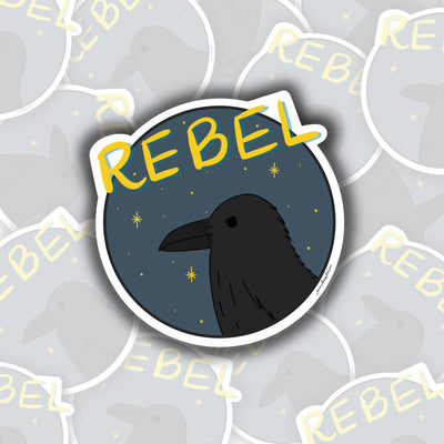 In the forefront of the sticker is a black raven facing the left. in the background is a navy blue sky with yellow stars. across the top of the sticker is yellow wording that says "rebel"