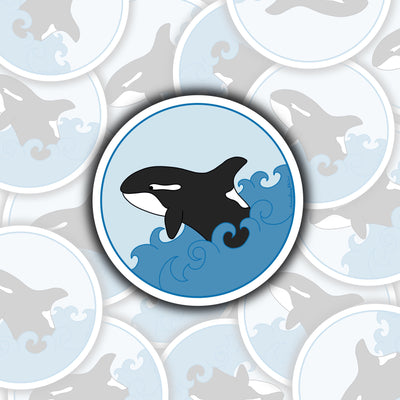 in the center of the sticker is a black and white killerwhale with dark blue waves coming up on either side of it. it has a light blue background.